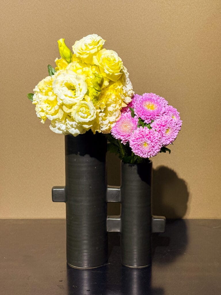 トルコキキョウとキクを使った、生け花とフラワーアレンジメントの融合作品。モダンな二連筒型花器に、左右対比で花をまとめた構成。 Ikebana arrangement with lisianthus and chrysanthemums in a modern dual-cylinder vase, blending traditional ikebana and floral arrangement styles.  