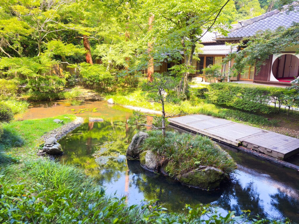 明月院の本堂奥に広がる池泉回遊式庭園と悟りの窓のある建物 / Scenic inner garden of Meigetsuin with pond and the building featuring the Window of Enlightenment  