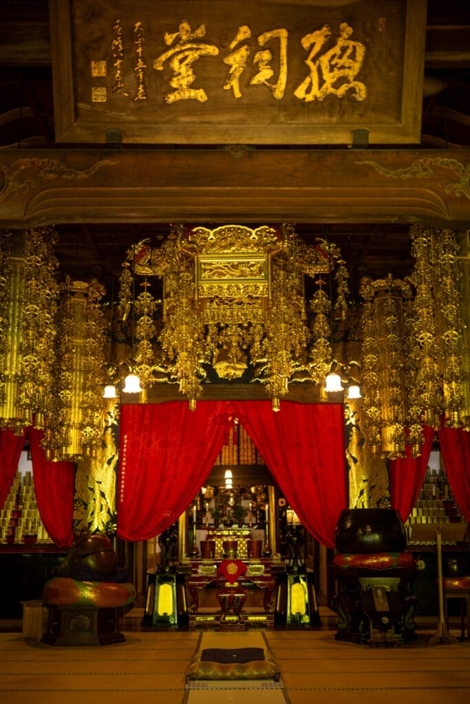永平寺の法堂内の荘厳な本尊と金色の装飾、赤い幕に包まれた神聖な空間 