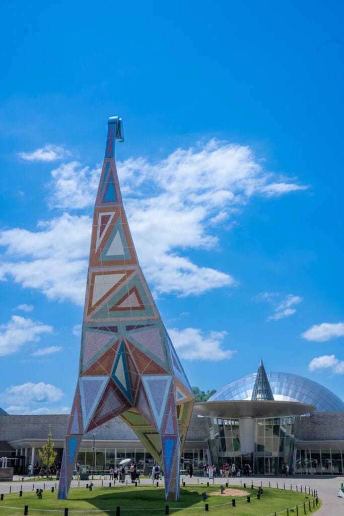 福井県立恐竜博物館の外観と恐竜をかたどったモニュメント。青空と白い雲に映える建物とシンボルが来館者を出迎える風景